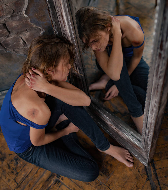 Nő áldozata a családon belüli erőszak és a bántalmazás sír és ül a padló közelében tükör, zúzódások és őt arc- és a sebek. Szemközti nézet. - Fotó, kép