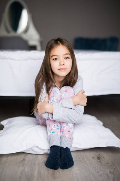 Portrait d'une petite fille déprimée bouleversée assise sur le sol près du lit le matin
 - Photo, image