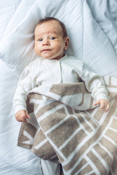 Cute funny baby lying on a white bed covered with a blanket. The concept of The tenderness of motherhood and family values - Photo, Image
