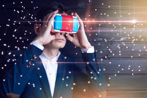 Jovem empresário atraente em terno usa um colorido óculos de realidade virtual em um fundo escuro. O conceito de tecnologia futurista e moderna em nossas vidas
 - Foto, Imagem