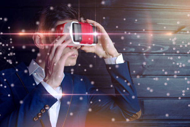 Atractivo joven hombre de negocios en traje utiliza unas gafas de realidad virtual de colores sobre un fondo oscuro. El concepto de tecnología futurista y moderna en nuestras vidas
 - Foto, imagen