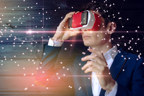 Aantrekkelijke jonge zakenman in pak gebruikt een kleurrijke VR-bril op een donkere achtergrond. Het concept van futuristische en moderne technologie in ons leven - Foto, afbeelding