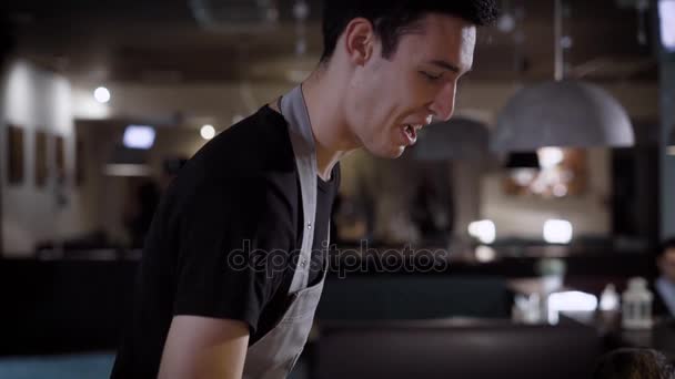 a friendly and smiling waiter advises the restaurant guests dishes for dinner, in a public place good service - Imágenes, Vídeo