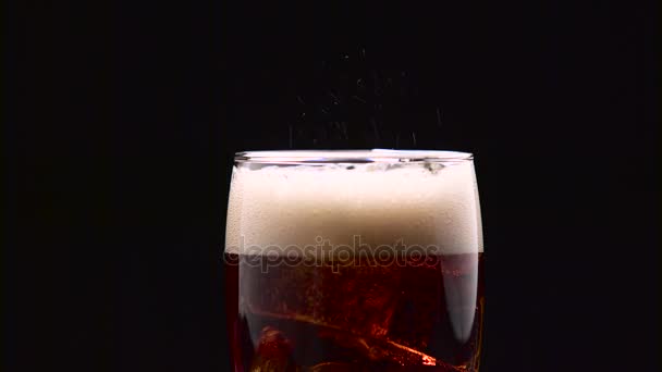 Glass of cola with ice hisses and foams on a black background. Close up - Felvétel, videó
