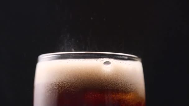 Sizzling white foam in a glass of cola on black background. Close up - Video
