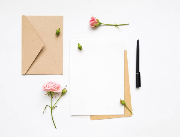 Letter and eco paper envelope on white background. Invitation cards, or love letter with pink roses. Holiday concept, top view, flat lay - Valokuva, kuva