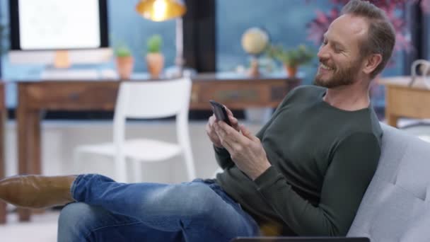 4K Happy man relaxing at home texting or using internet on his smartphone - Video