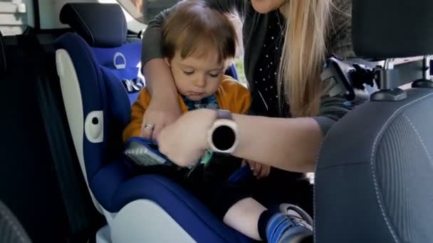 4 k video van jonge glimlachend aanpassen riemen van de moeder op haar childs veiligheid autostoel - Video