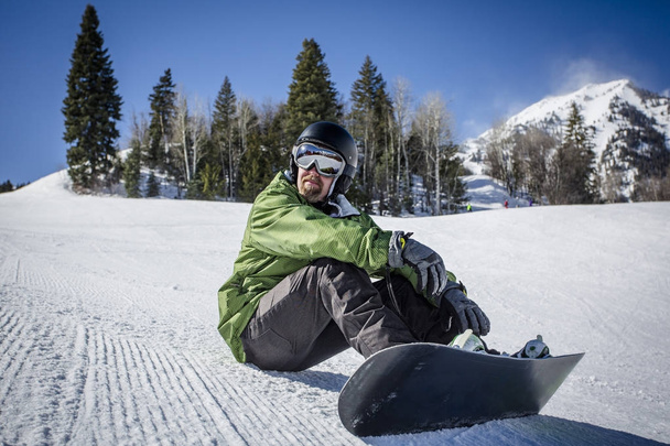 Αρσενικά ενήλικα snowboarder απολαμβάνοντας μια μέρα σε χιονοδρομικό θέρετρο, ενώ το υπόλοιπο σε μια τέλεια περιποιημένα σκι πλαγιά. Μια όμορφη μέρα στις πλαγιές τη διασκέδαση - Φωτογραφία, εικόνα
