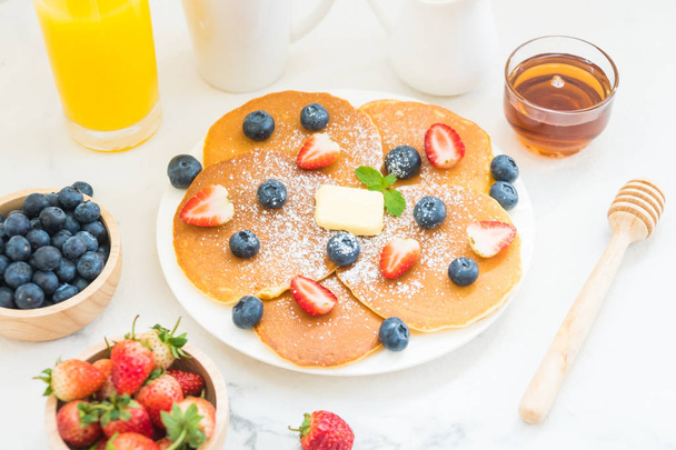 Zdravá snídaně sada s Pancake borůvky a jahody ovoce a černá káva, mléko a pomerančový džus na pozadí bílý kamenný stůl - Fotografie, Obrázek