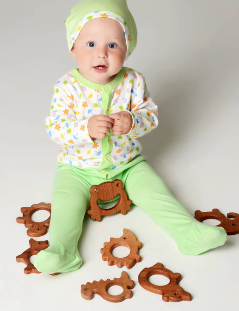 Infant child baby boy kid toddler sitting in light green body and hold wooden teether toy - Photo, Image