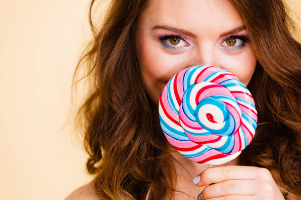 Woman holds colorful lollipop candy in hand, covering face - Φωτογραφία, εικόνα