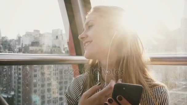 4K Happy Caucasian girl in Island Tramway, NY. Pretty lady with smartphone and earphones in a funicular. Sunlight flare. - Filmmaterial, Video