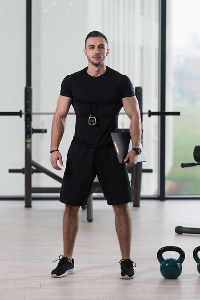 Personal Trainer In Sports Outfit Takes Notes On Clipboard In A Fitness Center Gym Standing Strong - Foto, Imagem