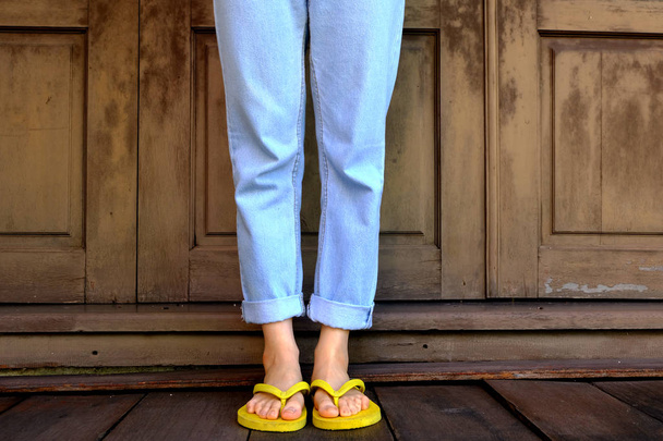 Yellow Flip Flops. Woman Legs and Feet Wearing Yellow Sandals Standing on Wooden Floor and wooden Wall Background Great for Any Use. - Фото, изображение