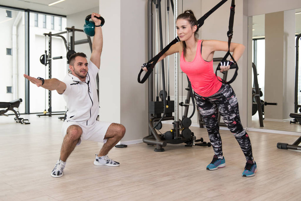 Personal Trainer Showing Young Woman How To Train With Trx Fitness Straps In The Gym - 写真・画像