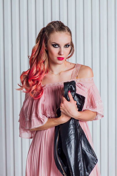Kaunis nuori nainen kirkas meikki ja vaaleanpunaiset hiukset nahkatakki ja vaaleanpunainen mekko poseeraa studiossa
. - Valokuva, kuva