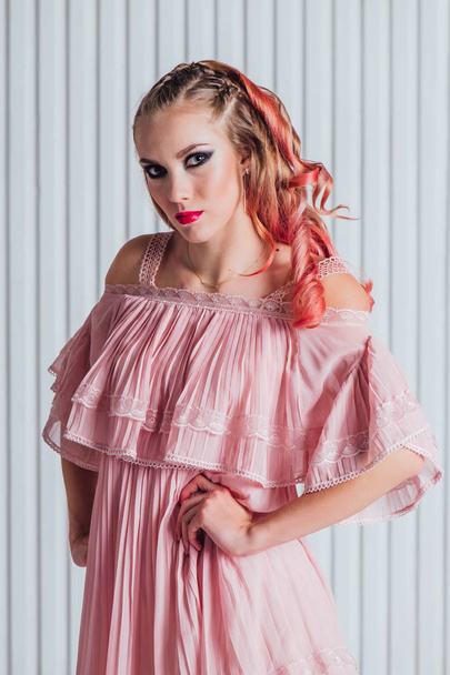 Beautiful young woman with bright make up and pink hair in and pink dress posing in studio. - Foto, afbeelding
