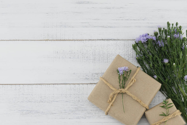 braune Geschenkboxen mit lila Ausstecher Blumen Strauß auf weißem Holz Hintergrund mit Kopierraum - Foto, Bild