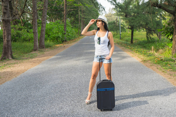 Young woman traveller in hat and with suitcase on the country road. - Φωτογραφία, εικόνα