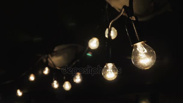 Luces decorativas de cuerda cuelgan y brillan al aire libre por la noche
 - Metraje, vídeo