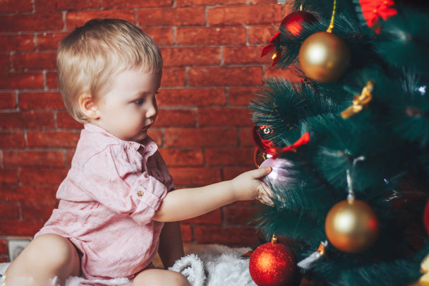 bebê tocando chistmas brinquedos na árvore de natal, ele tenta colocar bola na árvore
 - Foto, Imagem