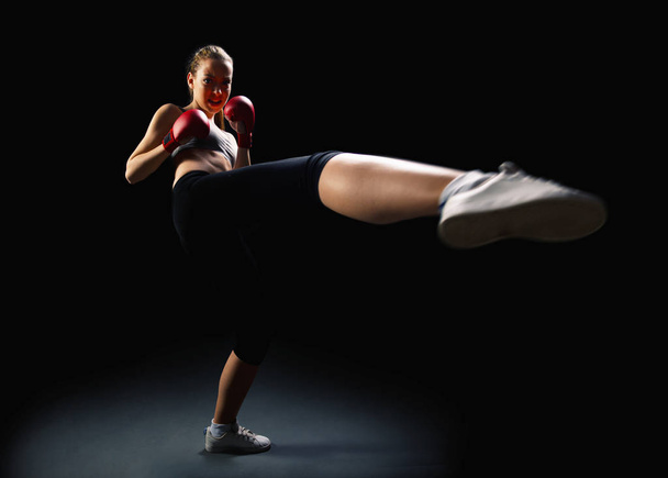 Energiek, fit, jonge vrouw kickboksen, zwarte achtergrond - Foto, afbeelding