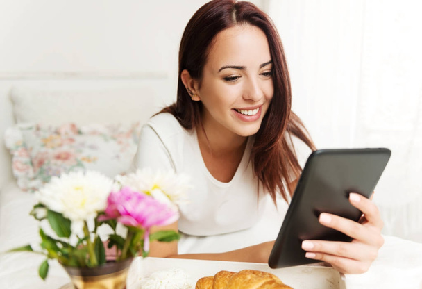 Beautiful woman using a tablet with breakfast in bed - Zdjęcie, obraz
