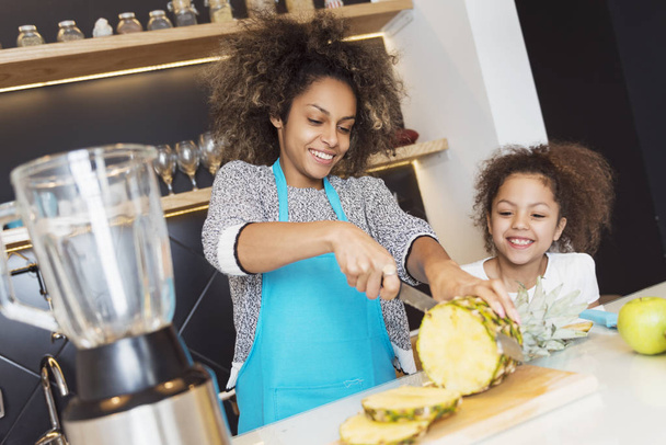Beautiful African American woman and her daughter making a smoothie in the kitchen - Foto, Bild
