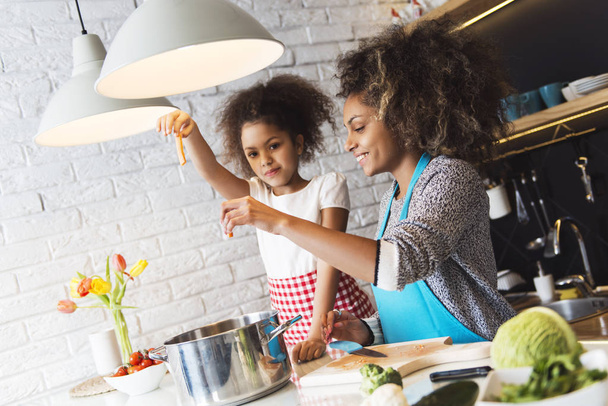Beautiful African American woman and her daughter cooking in the kitchen - Foto, Imagen