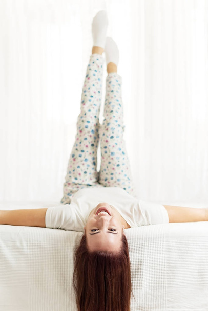 Beautiful, happy, woman laying on the bed in a bright room, enjoying - Фото, изображение
