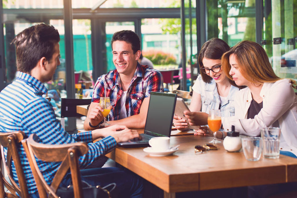 Gruppe junger Leute sitzt in einem Café und hält elektronische Geräte in der Hand - Foto, Bild