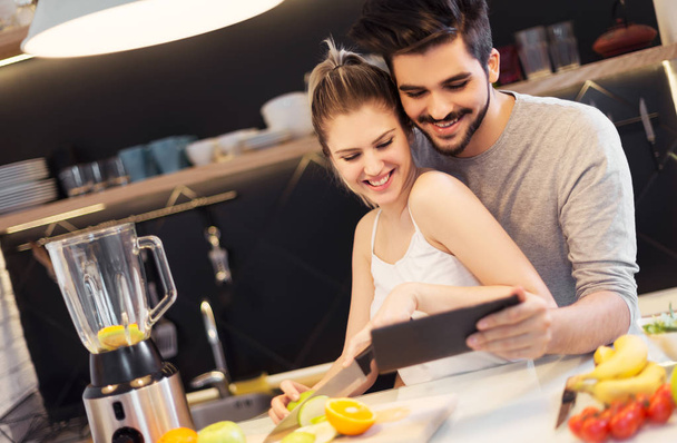 Young, romantic couple preparing food in the kitchen with tablet - Фото, зображення