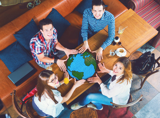 Group of young people pointing at planet Earth, sitting at the table.  - Photo, Image