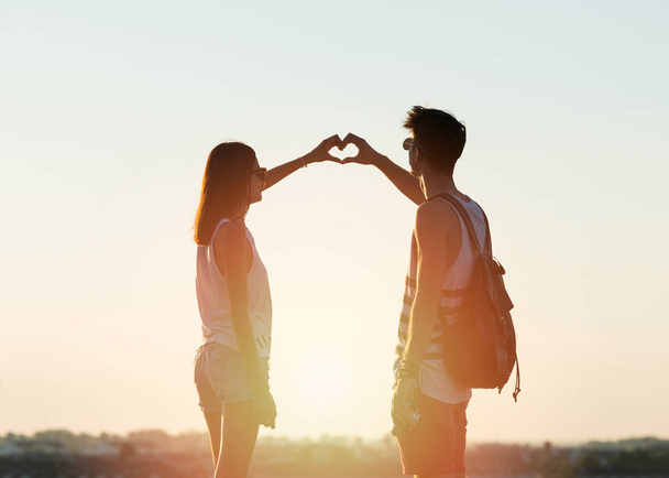 Two young people making a heart with their hands, sky and city in the background - Фото, изображение