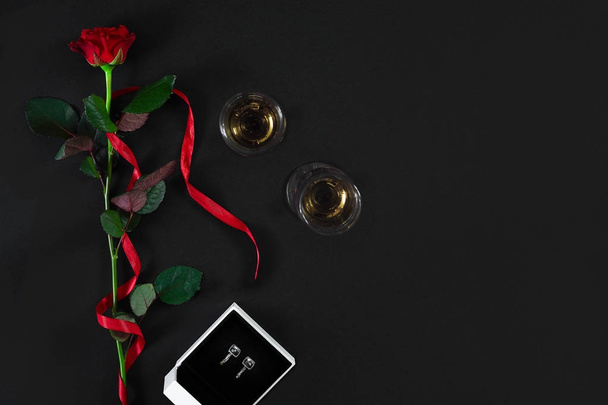 Одна темно-червона троянда з червоною стрічкою і коробкою з сережками на чорному
 - Фото, зображення