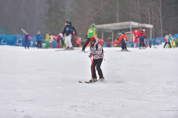 Жінка в лижному костюмі катається на лижах вниз з людьми на задньому плані
 - Фото, зображення