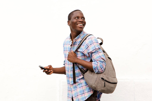 Portrét šťastný mladý muž chodit s vakem a mobilní telefon proti bílým pozadím - Fotografie, Obrázek