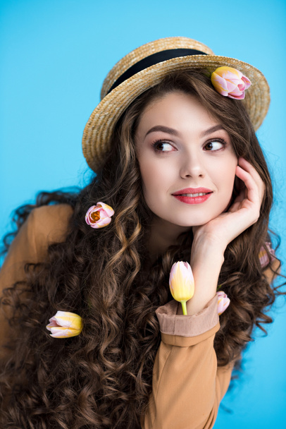 thoughtful young woman in canotier hat with tulips in her long curly hair - Foto, Bild