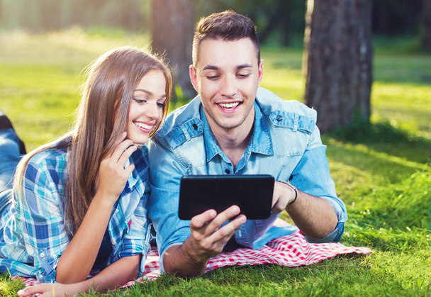 Two young people relaxing on the grass with tablet - 写真・画像