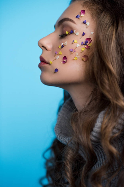 side view of young woman with flowers on face in sweater isolated on blue - Fotografie, Obrázek