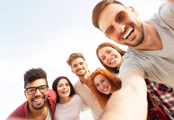 Grupo de jovens de pé em um círculo, ao ar livre, fazendo uma selfie
 - Foto, Imagem