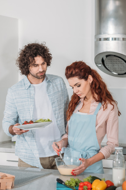 girlfriend preparing batter and boyfriend holding plate with vegetables - Photo, Image