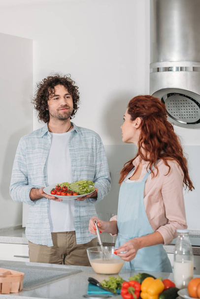 girlfriend preparing batter and boyfriend holding plate with vegetables - Photo, Image