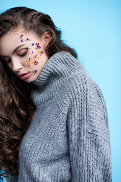 attractive young woman with flowers on face in warm grey sweater isolated on blue - Fotografie, Obrázek