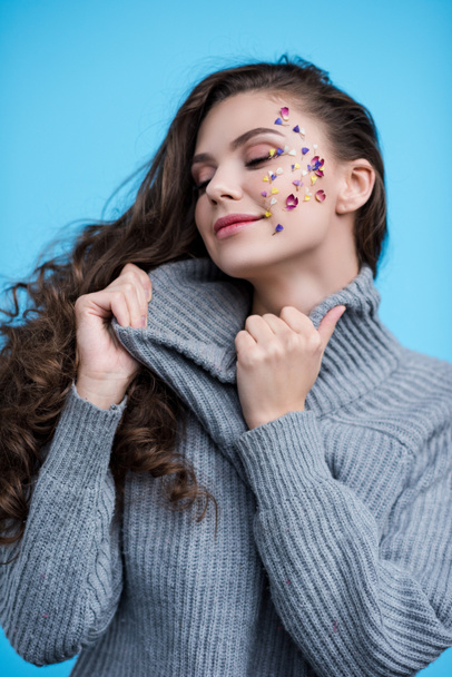 woman with flowers on face stretching neck of stylish sweater isolated on blue - Zdjęcie, obraz