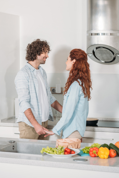 happy couple holding hands and looking at each other at kitchen - Фото, зображення