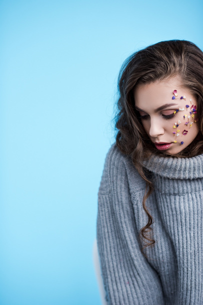 beautiful woman in warm grey sweater and flowers on face isolated on blue - Photo, image