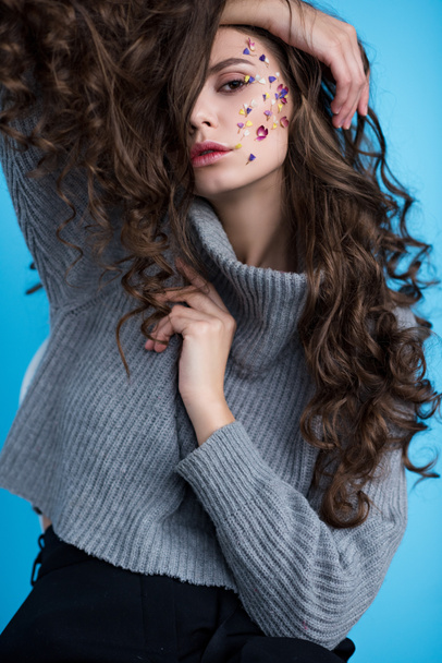 sensual young brunette woman with flowers on face looking at camera isolated on blue  - Fotografie, Obrázek