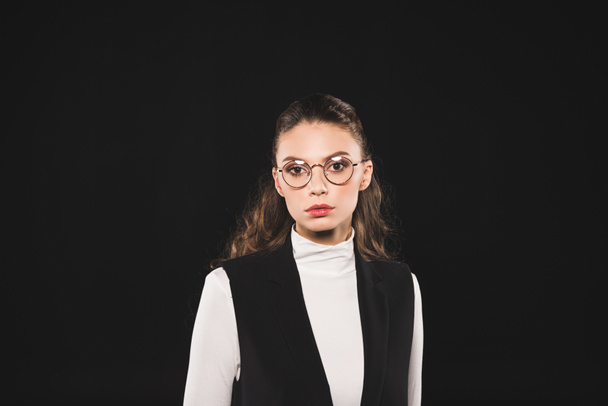 portrait of beautiful brunette woman in eyeglasses looking at camera isolated on black  - Fotografie, Obrázek
